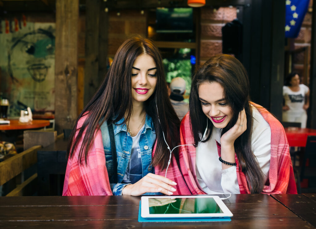 two young beautiful girl sitting table watching something tablet